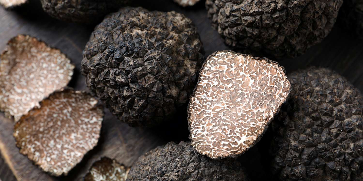 Whole and cut black truffles on wooden board, top view