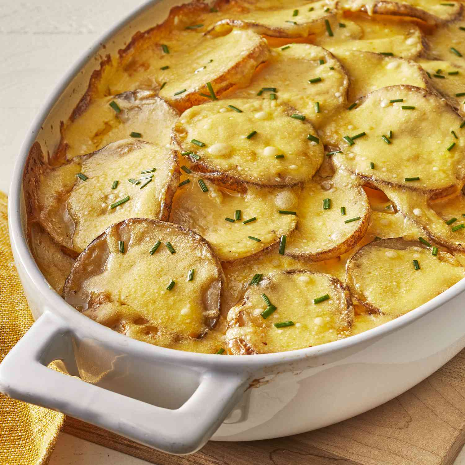a close up view of creamy au gratin potatoes in a white oval casserole dish topped with fresh chives