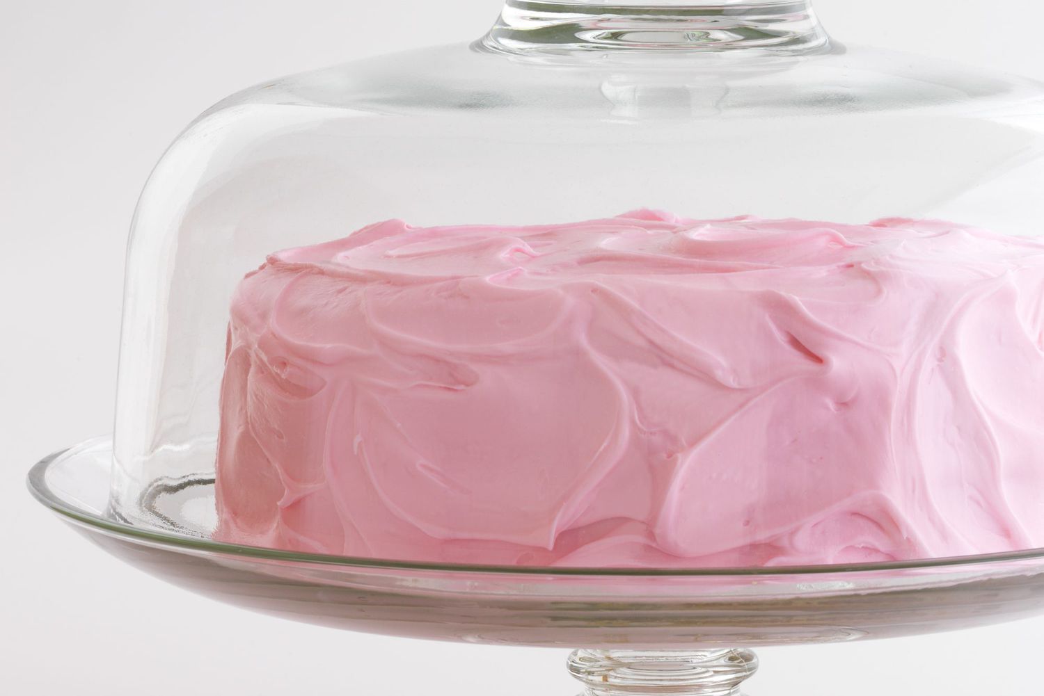 pink frosted cake in glass cake cover