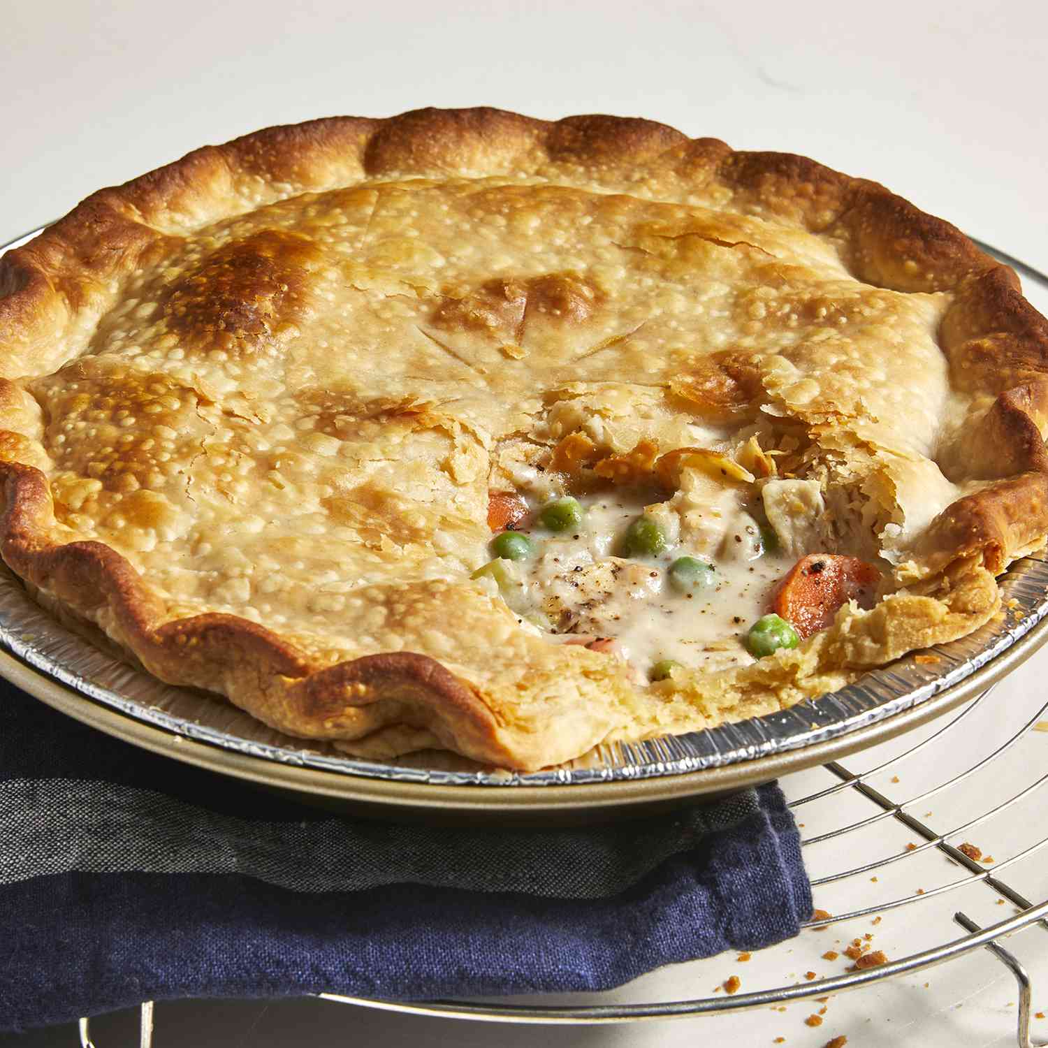 a low, close up view of a golden-brown chicken pot pie cooling on a rack, with a piece missing revealing the creamy hardy pie filling.