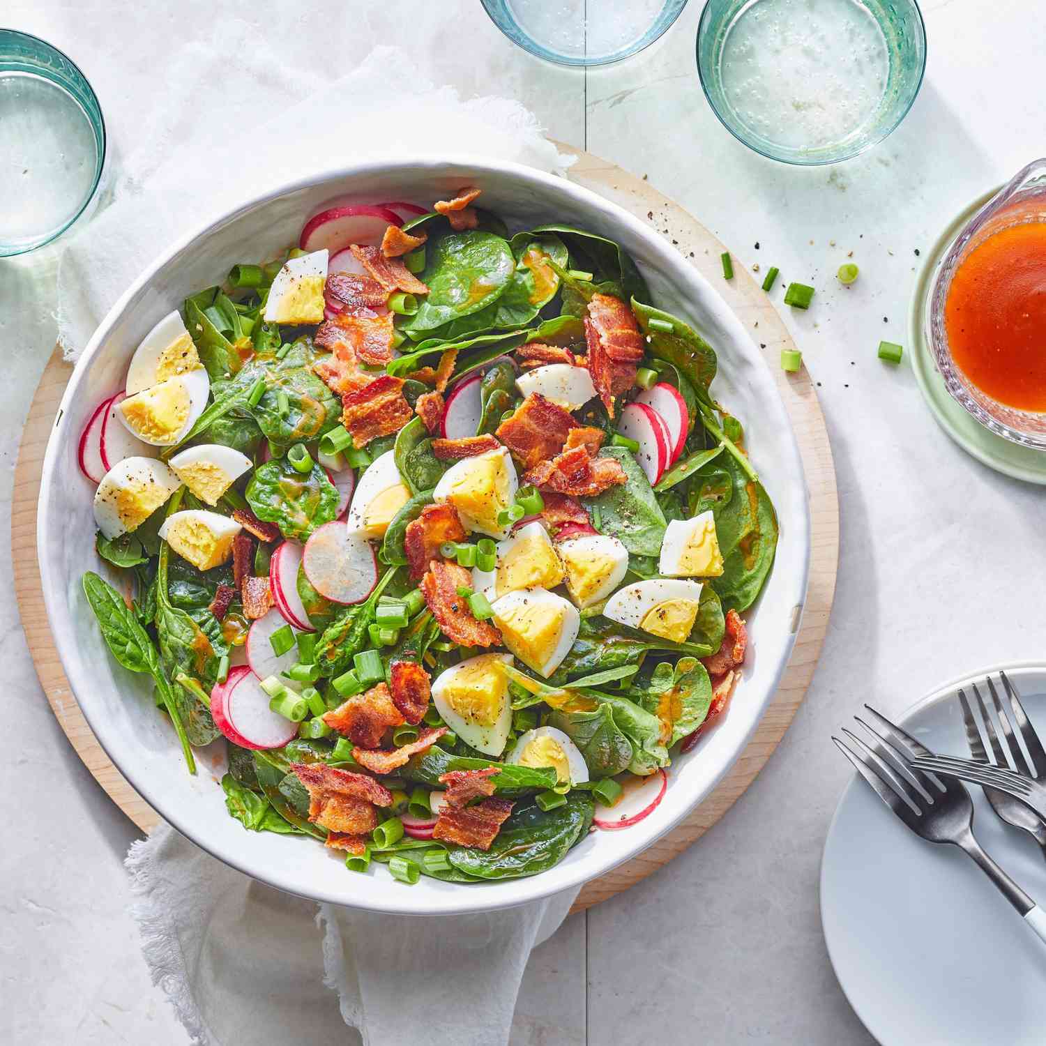 Spinach salad in a white bowl with bacon, eggs, radishes, and green onion