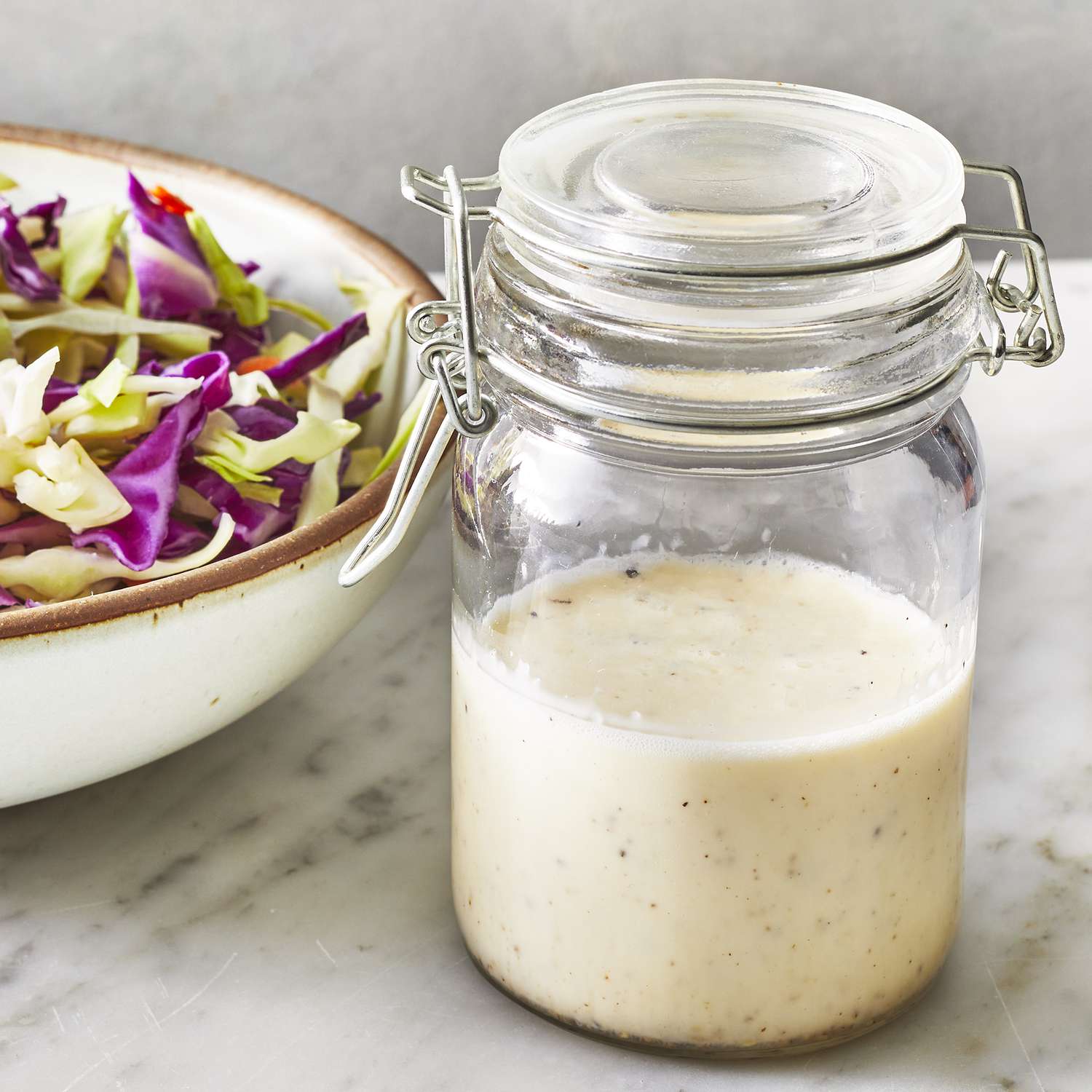 a low angle, close up view of a closed jar of coleslaw dressing with a bowl of shredded cabbage nearby