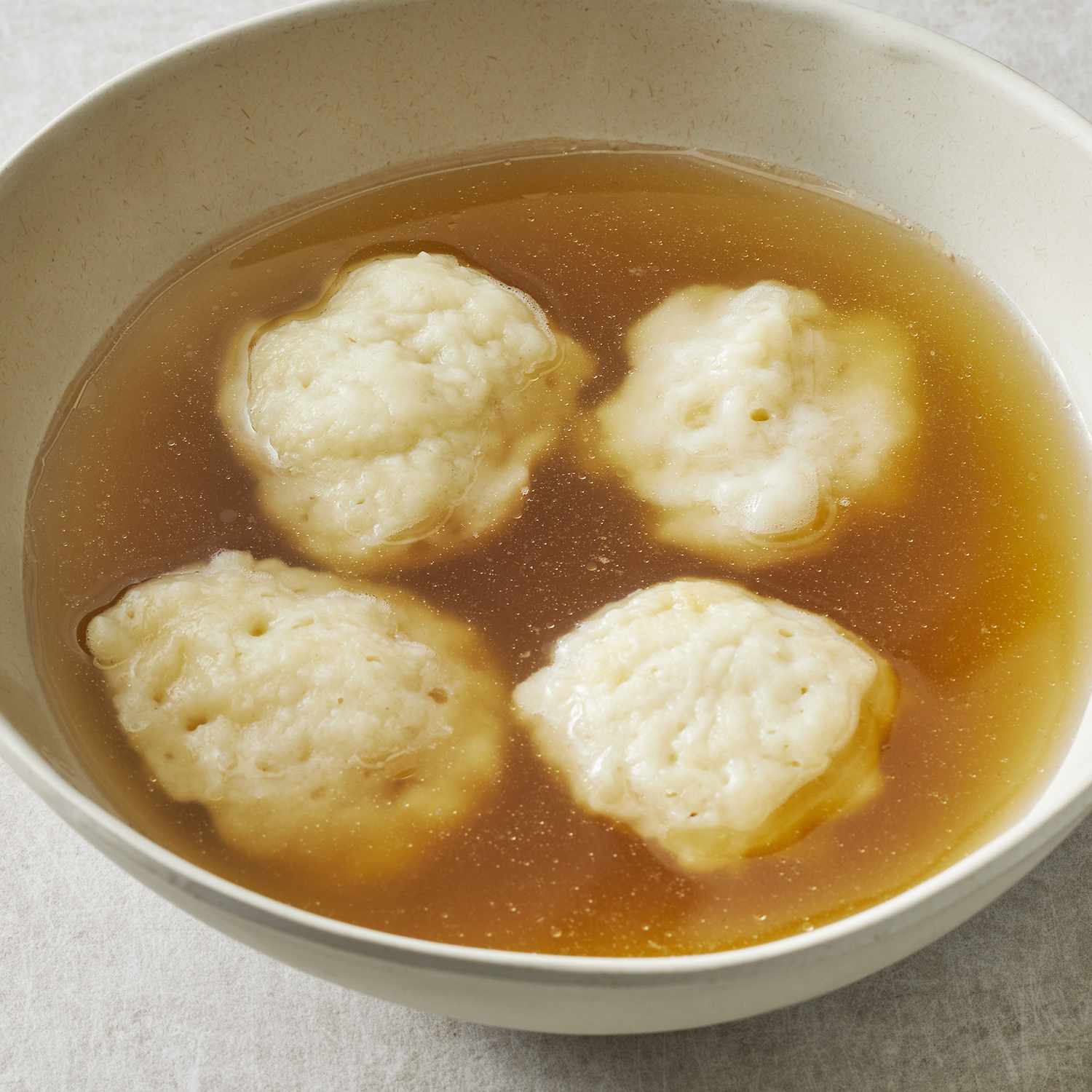 a close up view of a bowl with four fluffy dumplings in a clear broth