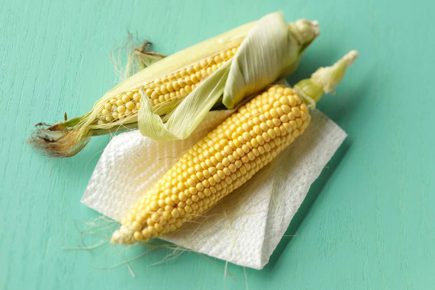 two corn on the cob sit beside each other on a paper towel on a blue background
