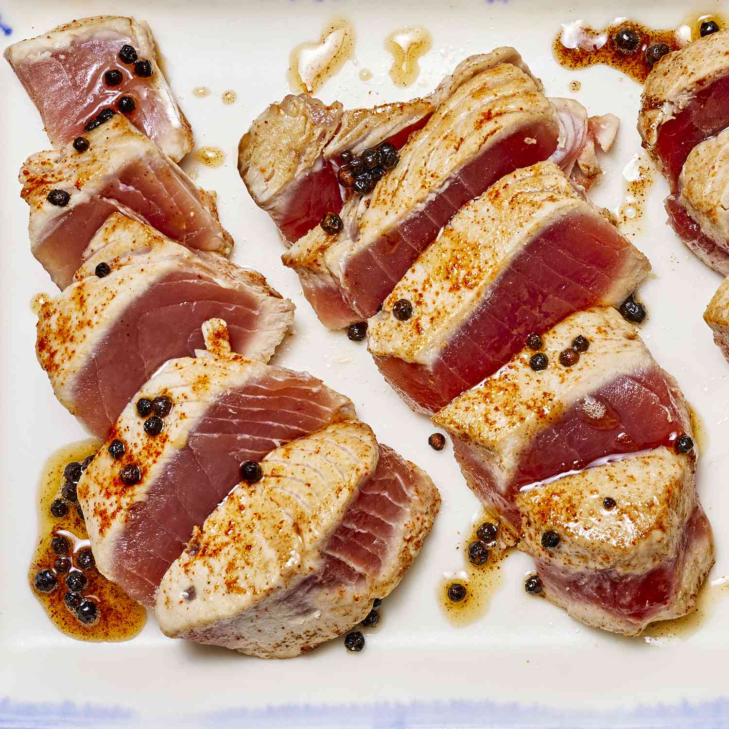 several medium rare seared tuna steaks are sliced on a blue and white platter.