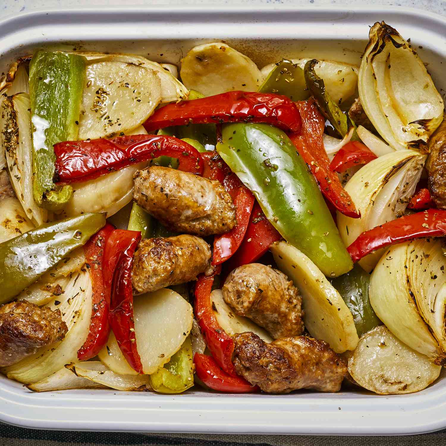 an overhead view of baked sausage, peppers, onions, and potatoes in a white baking dish.