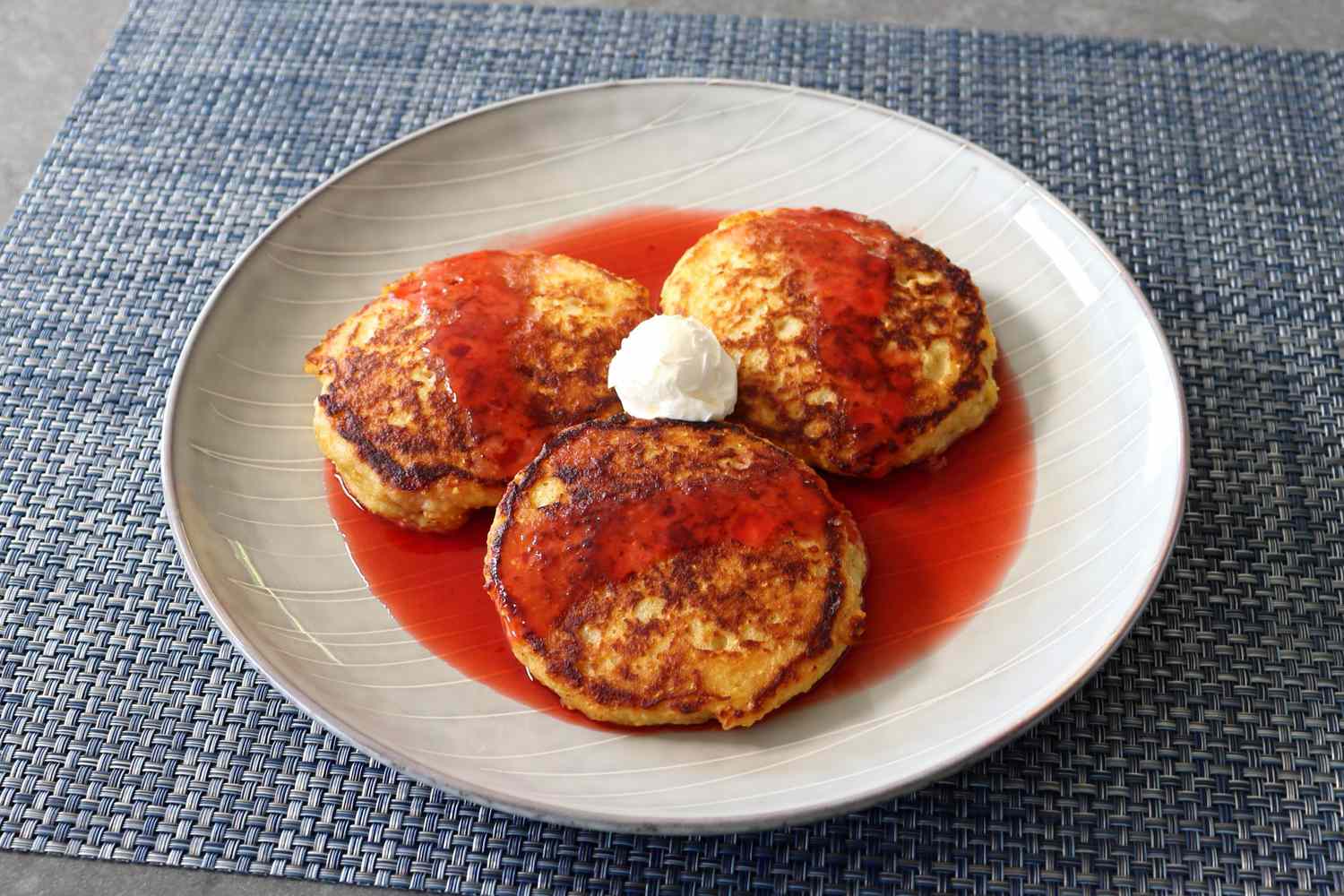 Three cornbread pancakes topped with a strawberry syrup on a white plate