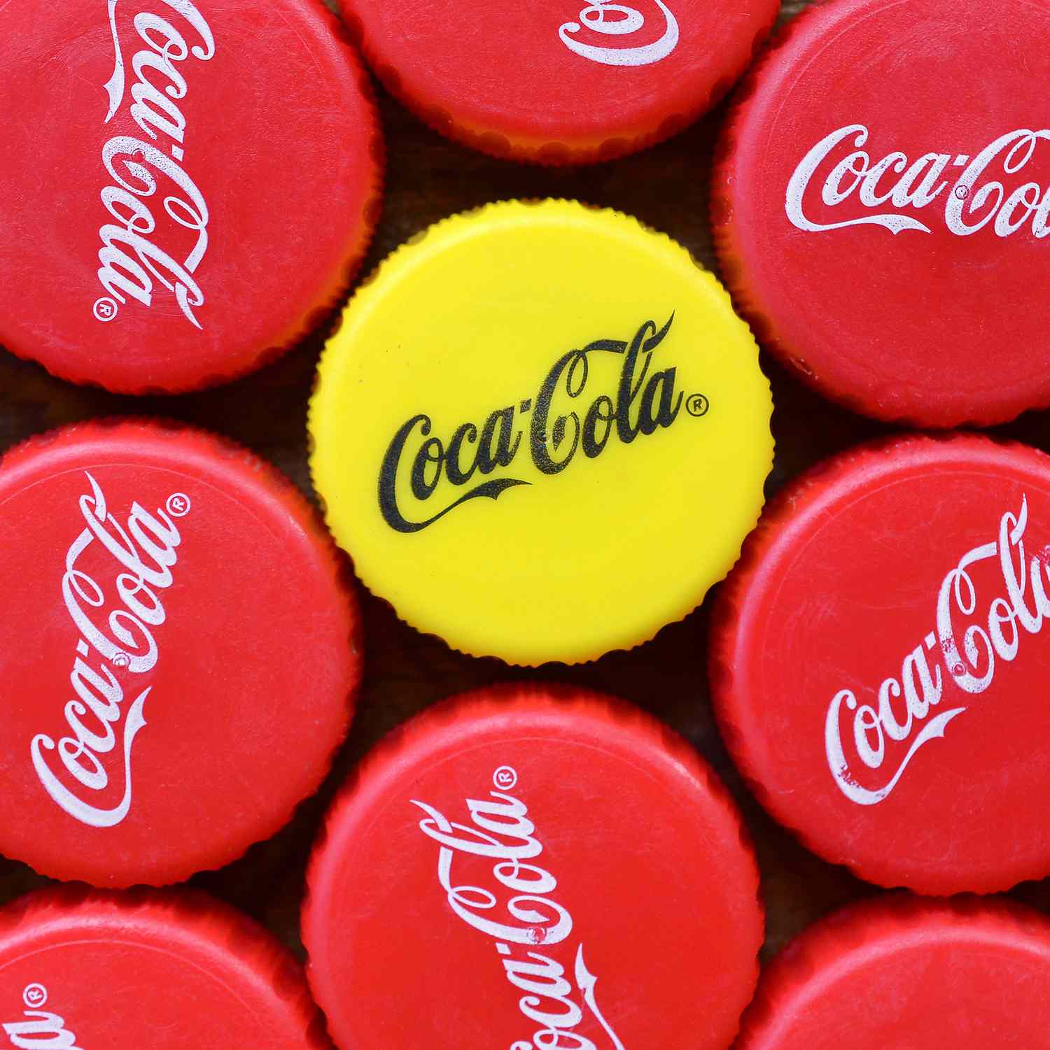 Many red lids and one yellow plastic cap with coca cola logo close up