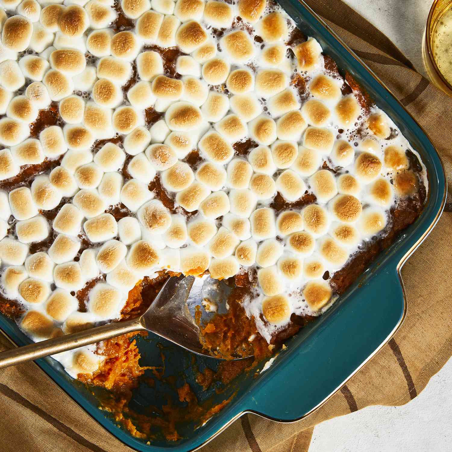 an overhead view looking into a candied sweet potato casserole topped with golden-brown marshmallows. a scoop has already been taken out.