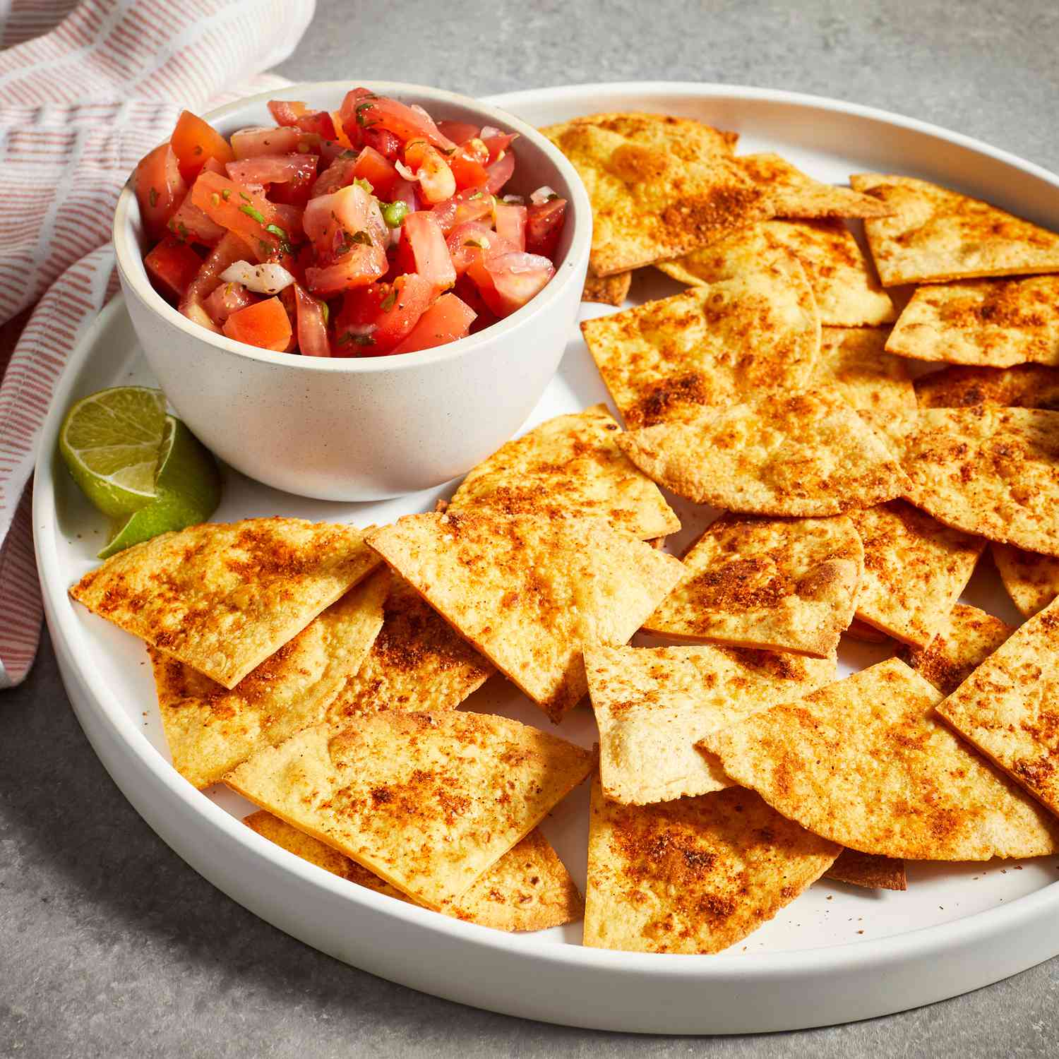 a low angle view of a platter of golden-brown baked tortilla chips served with a side of fresh salsa.
