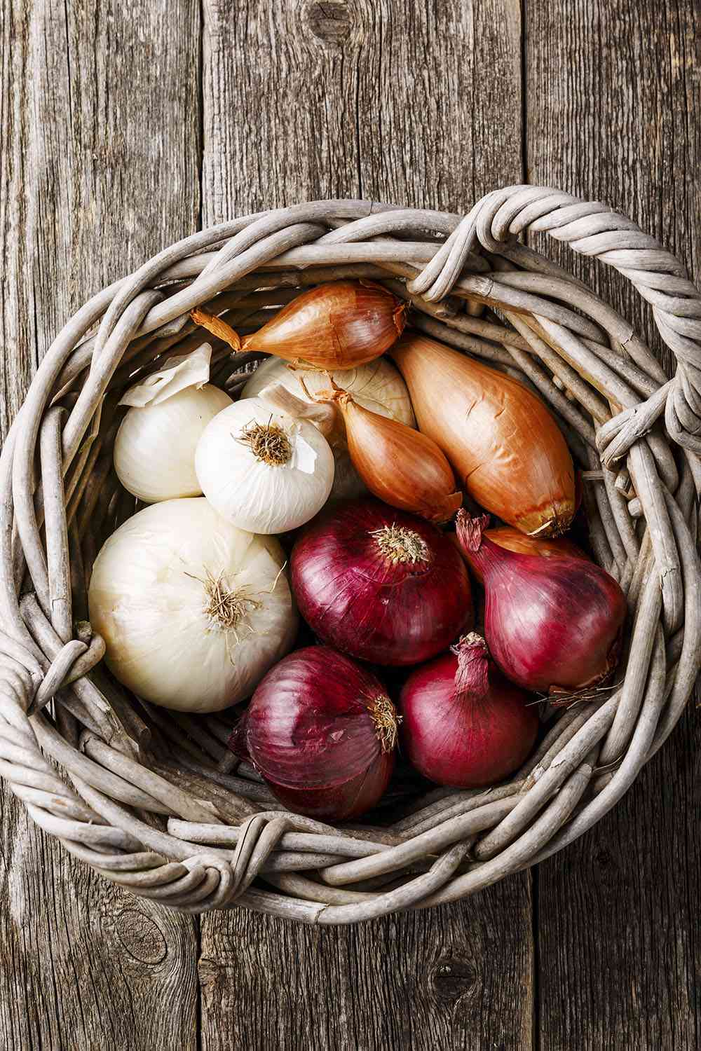 Different types of onions in basket on wooden background
