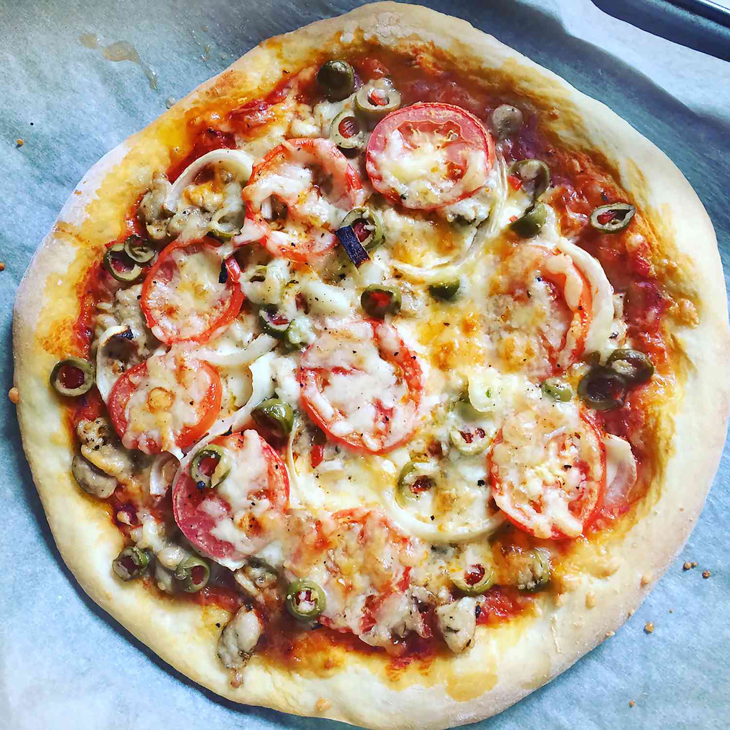 a top down view of a fresh baked homemade pizza topped with tomatoes, olives, onions, and mushrooms