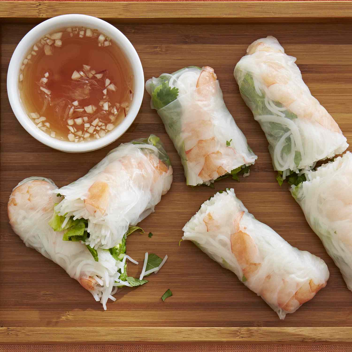 An overhead view of 3 Vietnamese Spring rolls, cut in half, on a bamboo tray. Served with a chili sauce