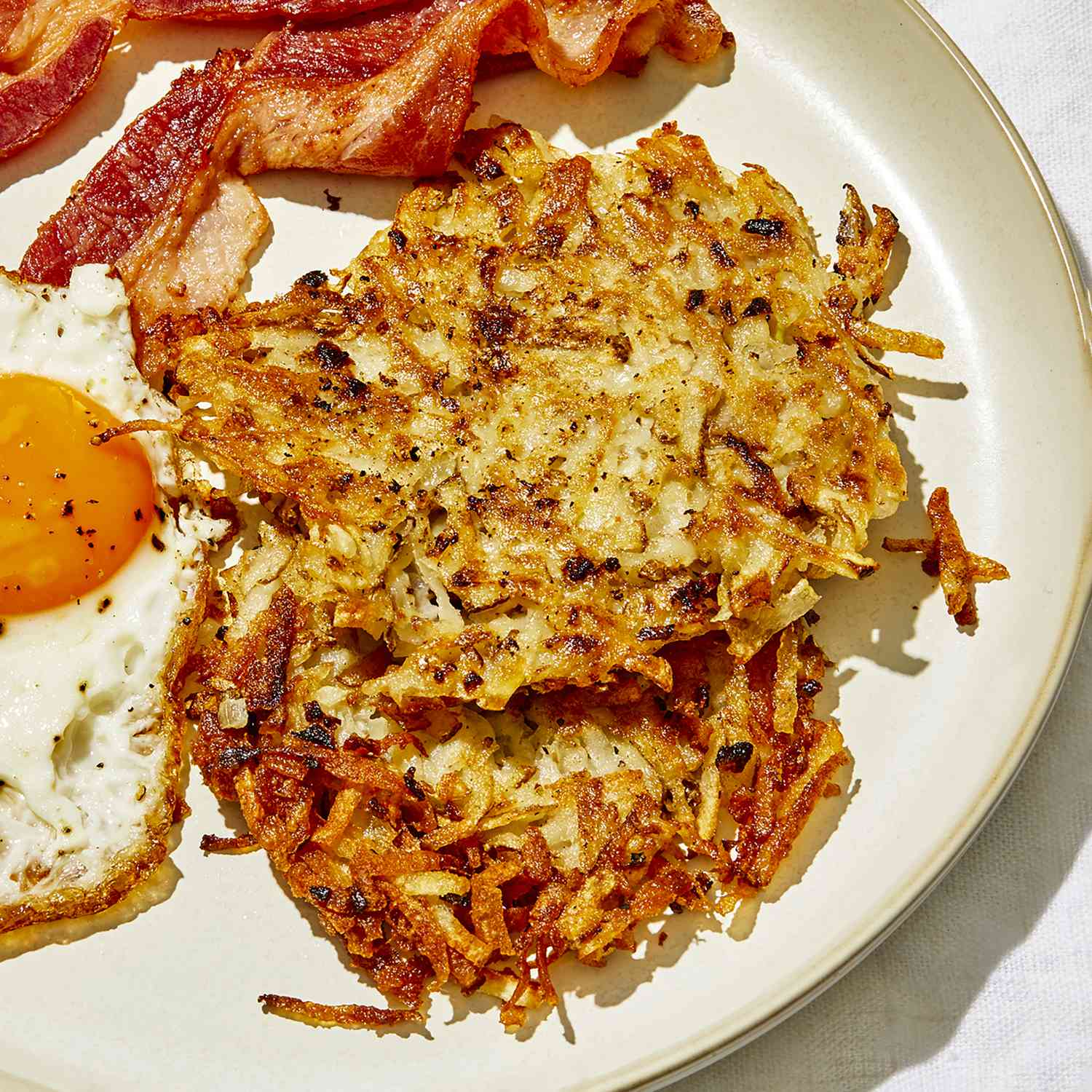 a close up view of two crispy hashbrown patties served with an over easy egg and crispy bacon