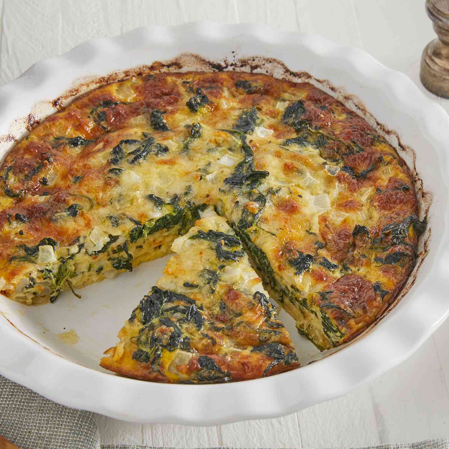slightly less than overhead angle, looking into a casserole dish of a sliced spinach quiche and a slice off to the side