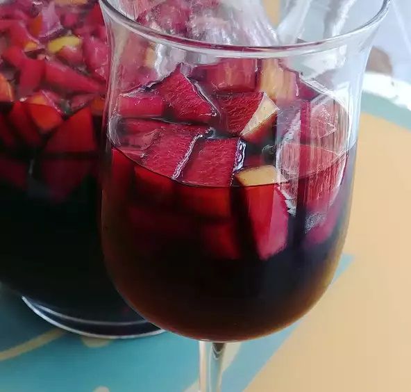 a glass of fruit-filled red wine sangria with a pitcher of sangria in the background