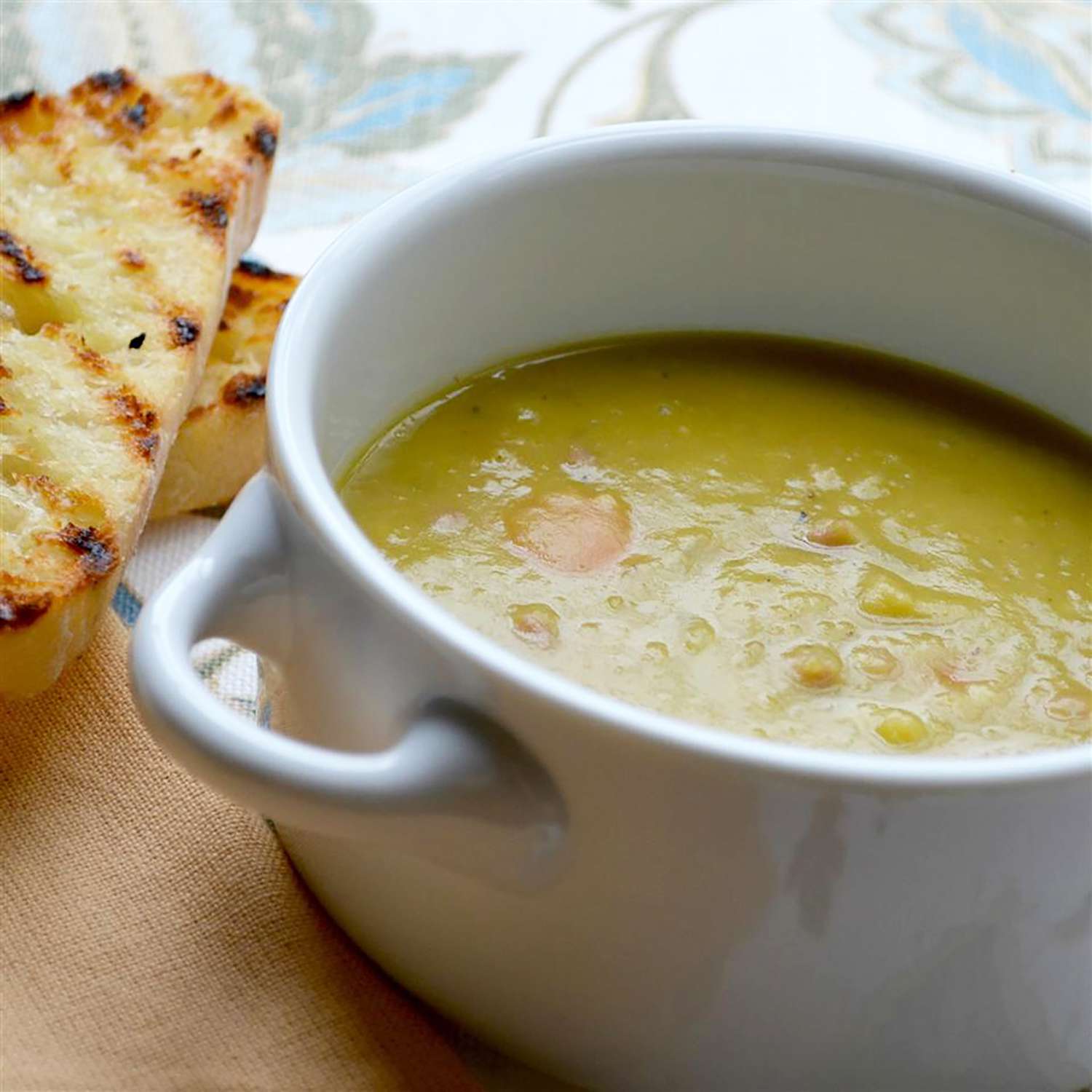 close up view of a bowl of ham and split pea soup in a bowl, with toasted bread on the side