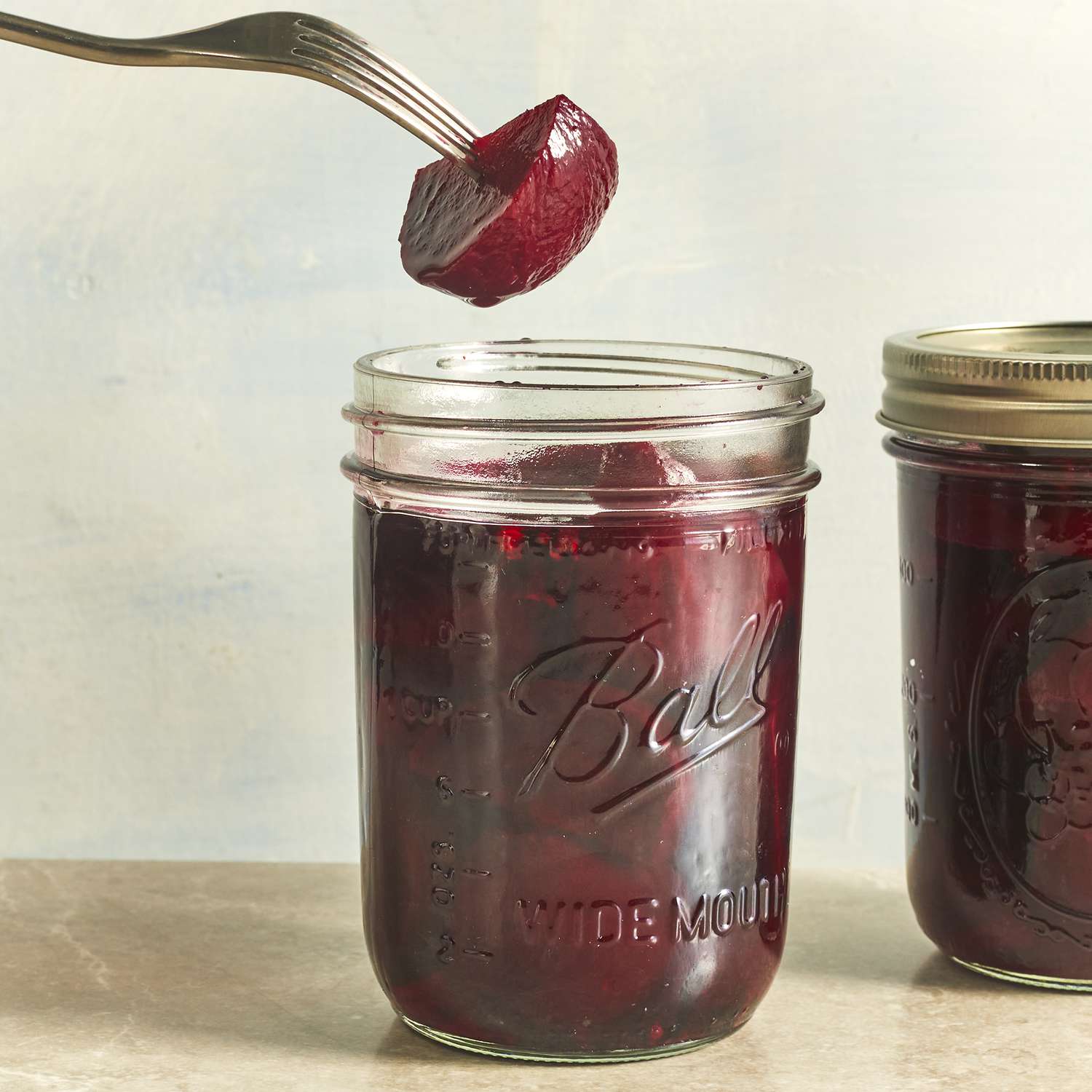 close up image of a beet on a fork and beets in jars