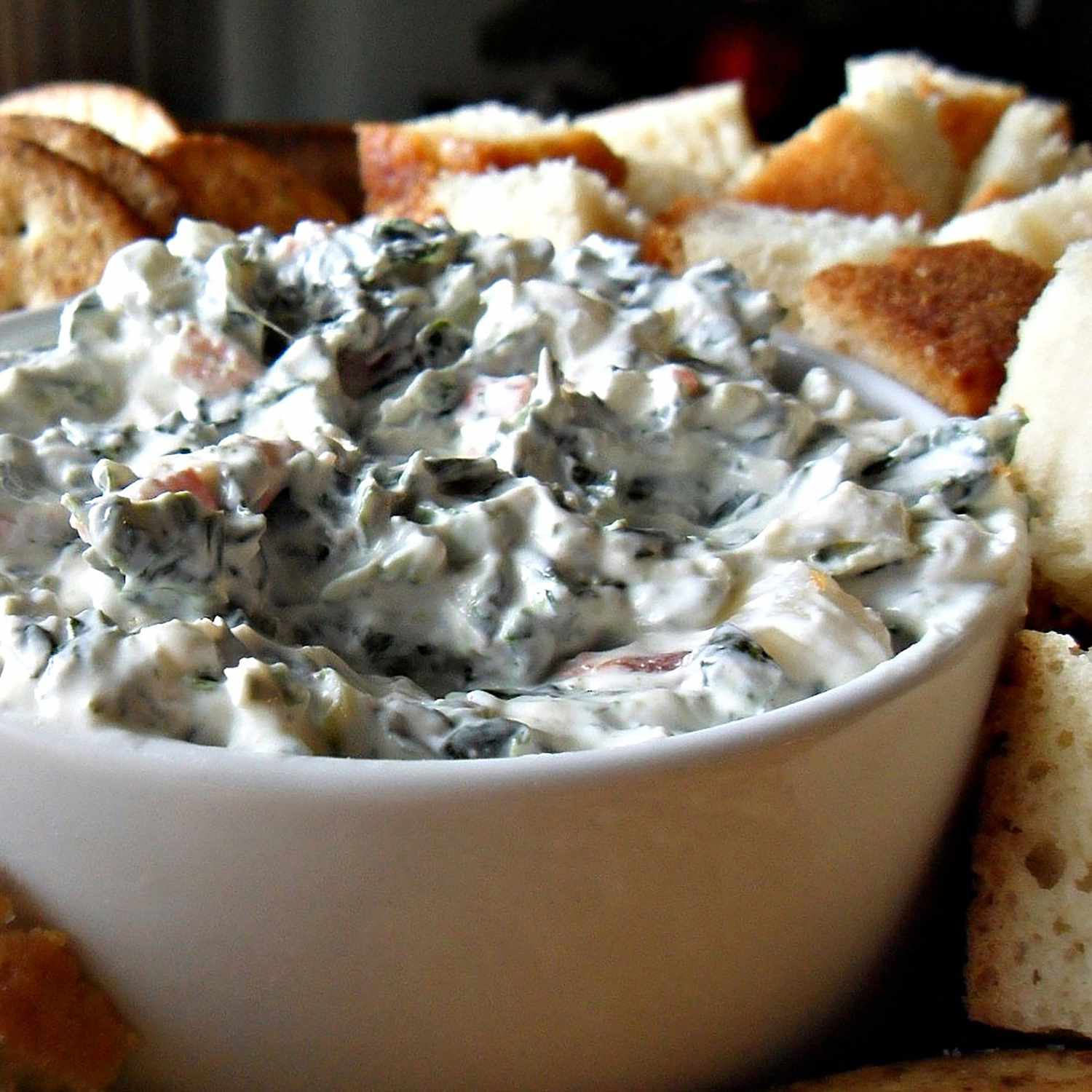 Close up view of spinach dip in a bowl, with bread cubes and crackers on the side