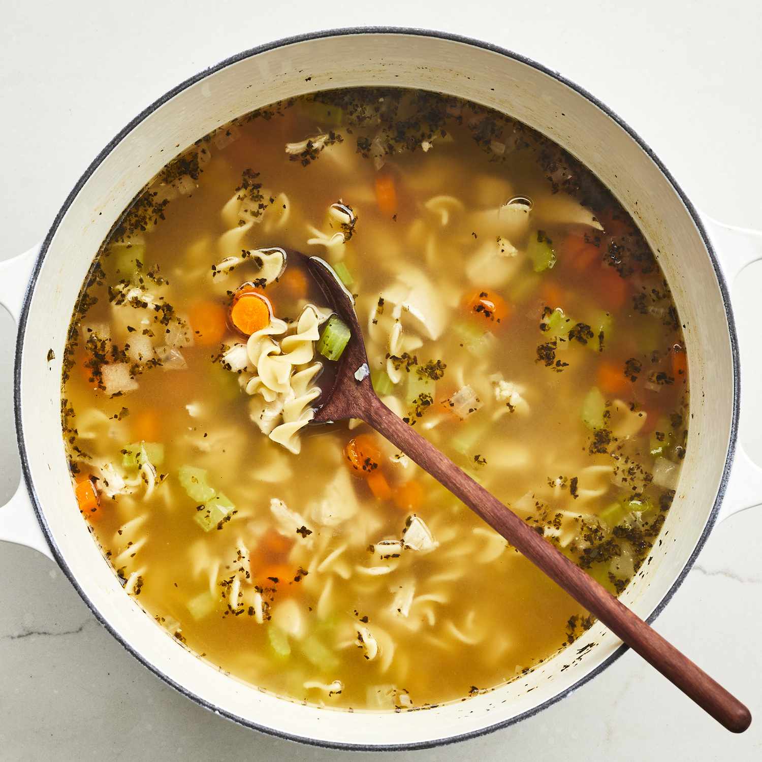 close up view of chicken noodle soup in a pot with a wooden spoon