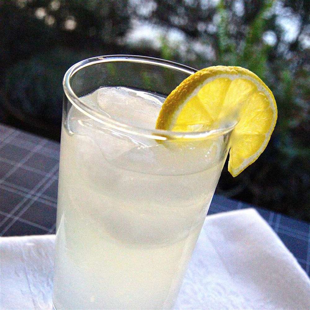 close up view of a glass of tom collins cocktail garnished with a slice of lemon