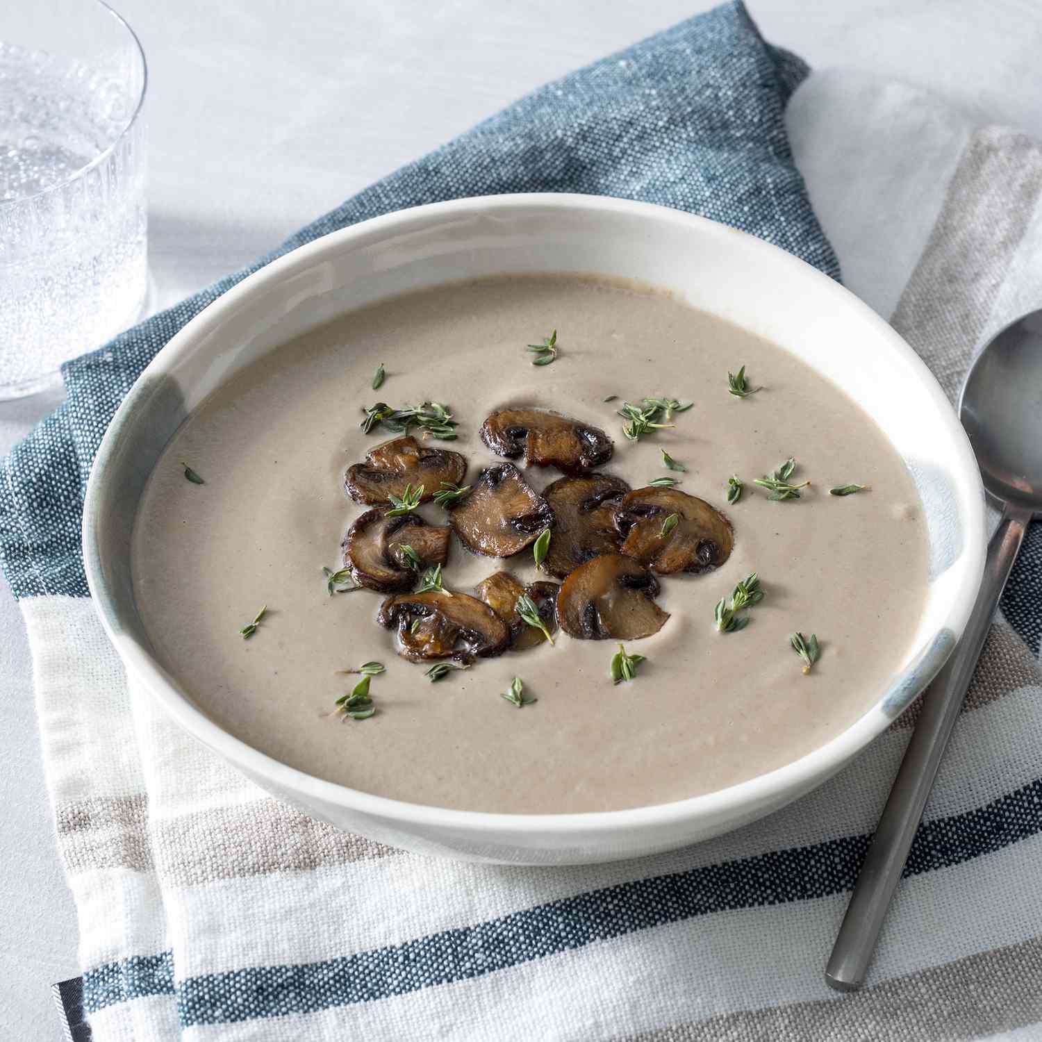 close up view of Creamy Mushroom Soup in a bowl on top of a kitchen towel, garnished with mushrooms and herbs