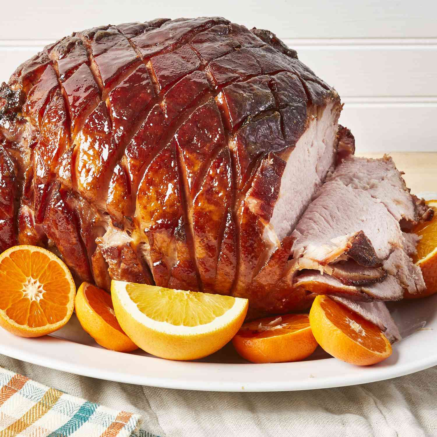 close up view of Tangy Honey-Glazed Ham sliced on one side, on a platter with citrus