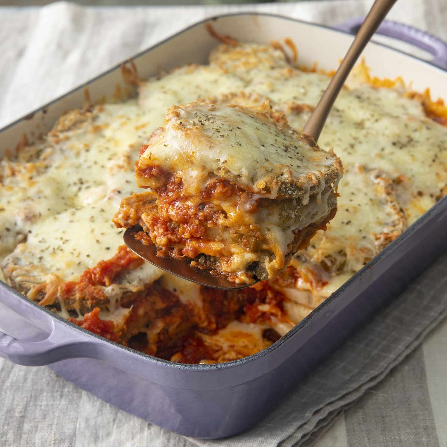 close up view of eggplant parmesan in a baking dish, and a slice of eggplant parmesan on a spatula