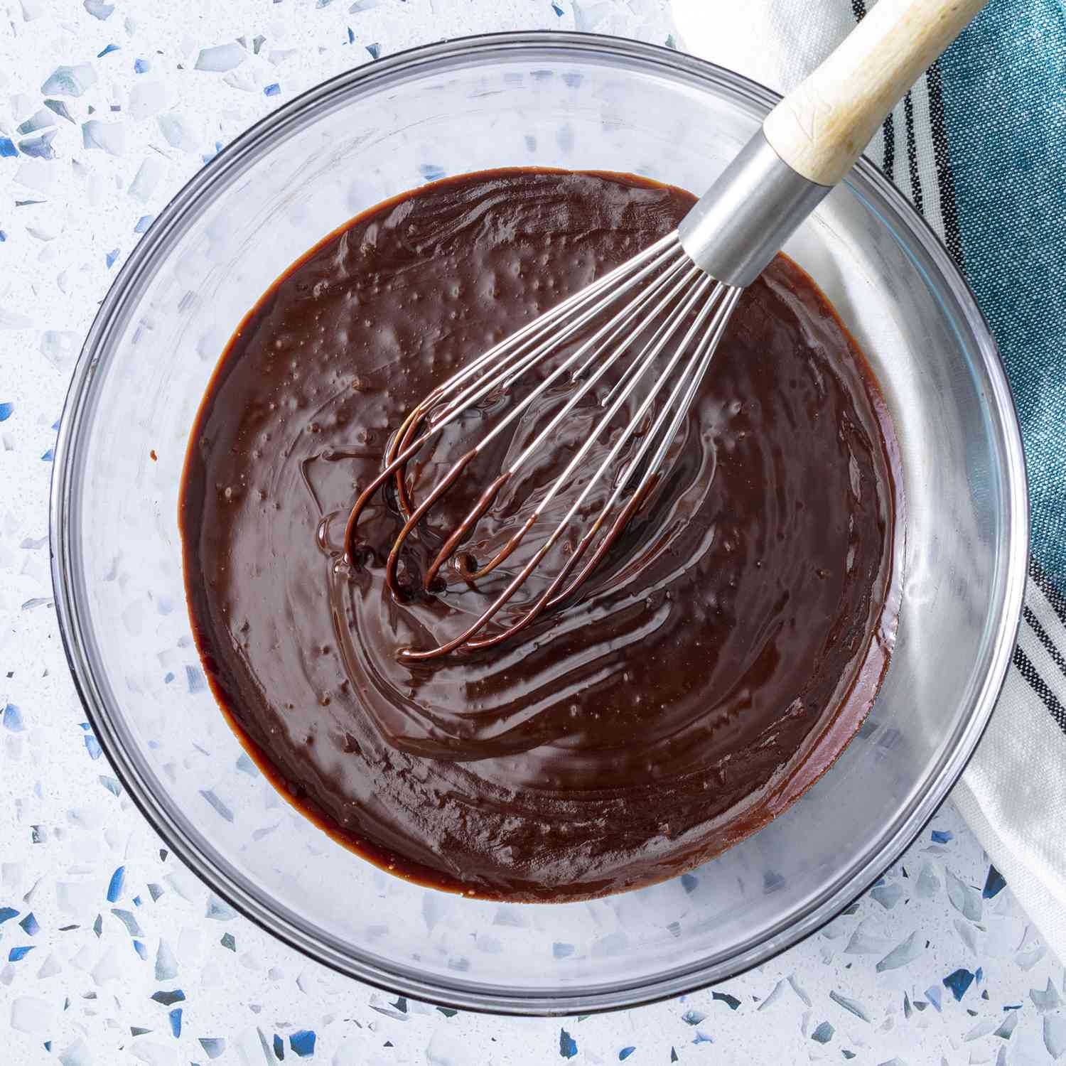 overhead shot of chocolate ganache in a glass bowl with a whisk
