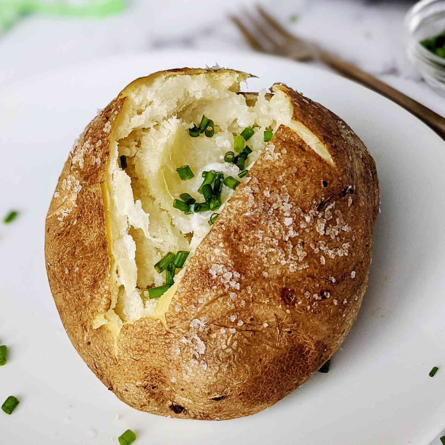 a close up view of a split baked potato dressed with salt, butter, and chives