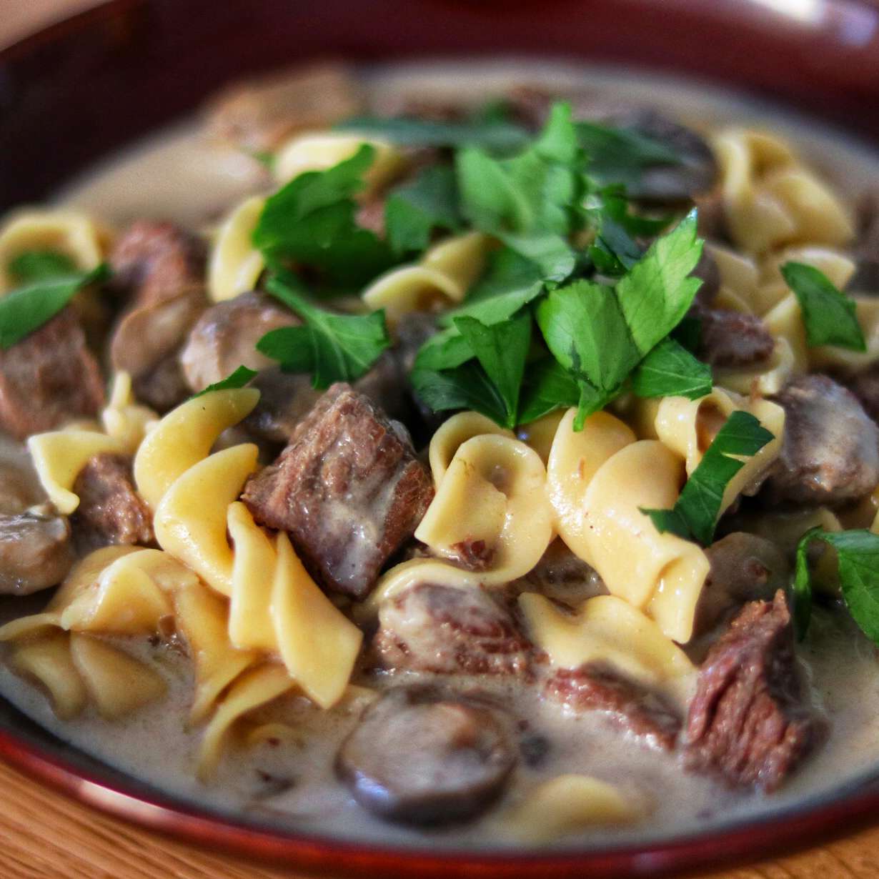 close up view of beef stroganoff in a bowl, with herbs on top