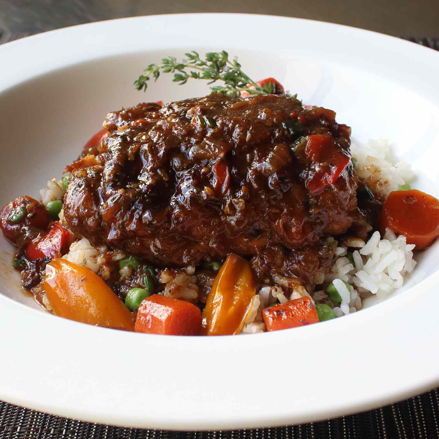 close up view of Jamaican Brown Stew Chicken in a bowl with rice, vegetables and herbs