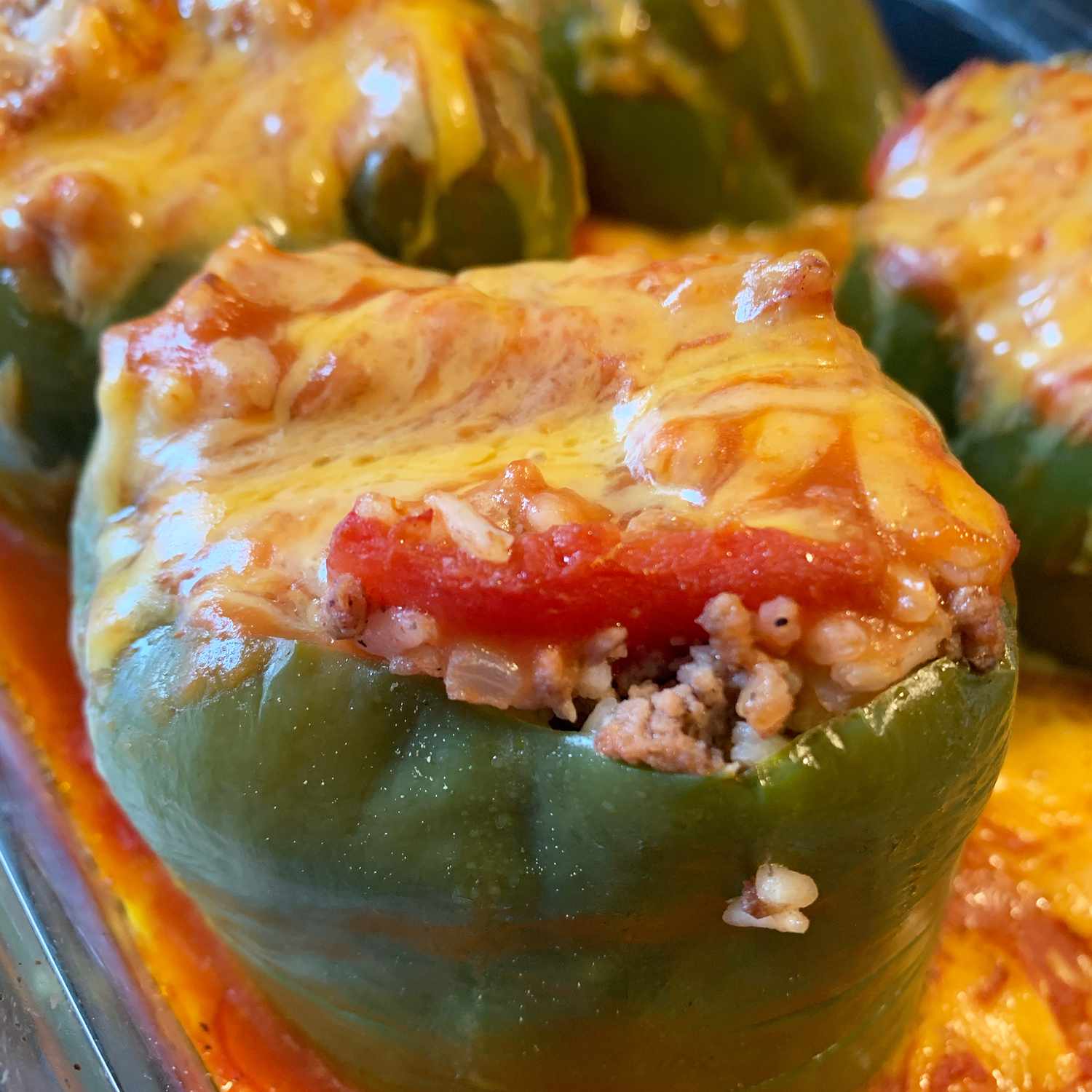 close up view of Stuffed Green Peppers with melted cheese on top, in a glass baking dish
