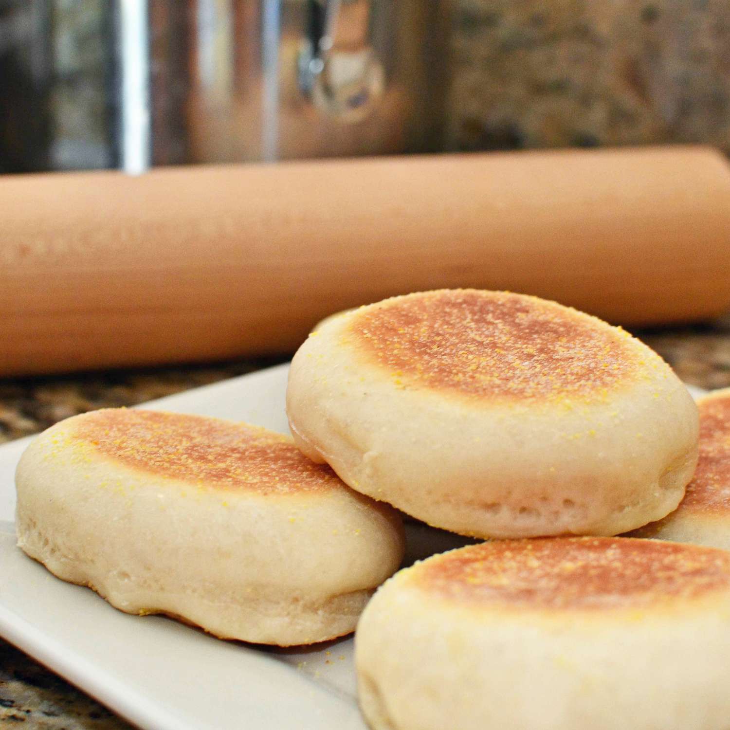 close up view of English Muffins on a plate with a wooden rolling pin in the background