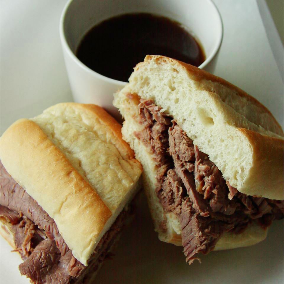 close up view of a sandwich and Easy Slow Cooker French Dip in a bowl in the background