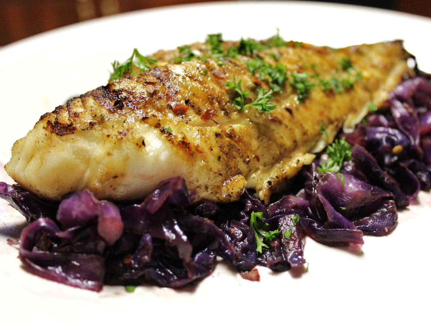 close up view of a Grilled Fish Steak garnished with herbs on a bed of red cabbage on a platter