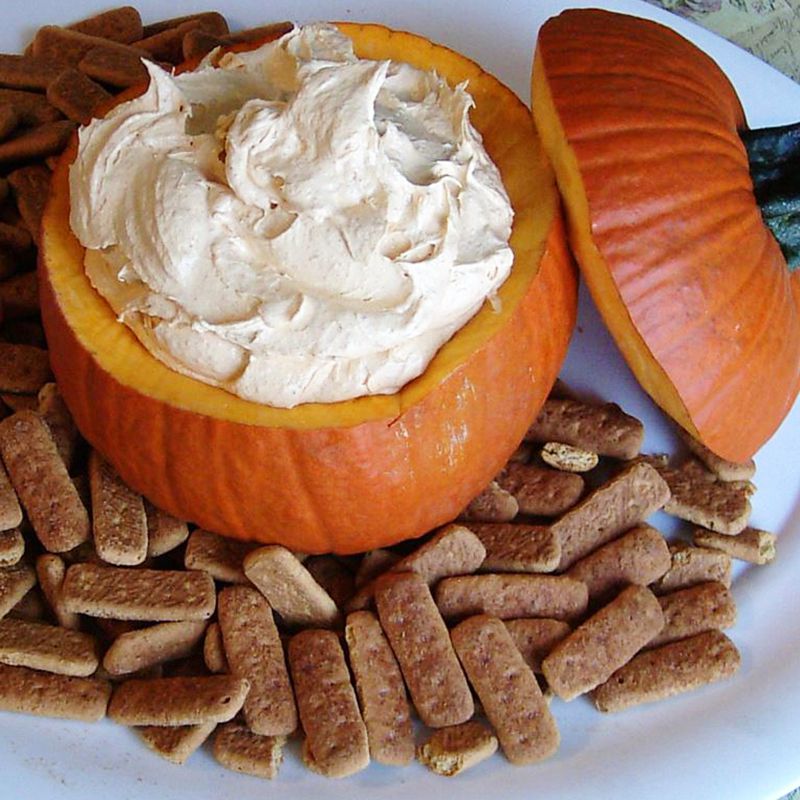 close up view of pumpkin fluff dip in a pumpkin and cookies surrounding the dip on a platter
