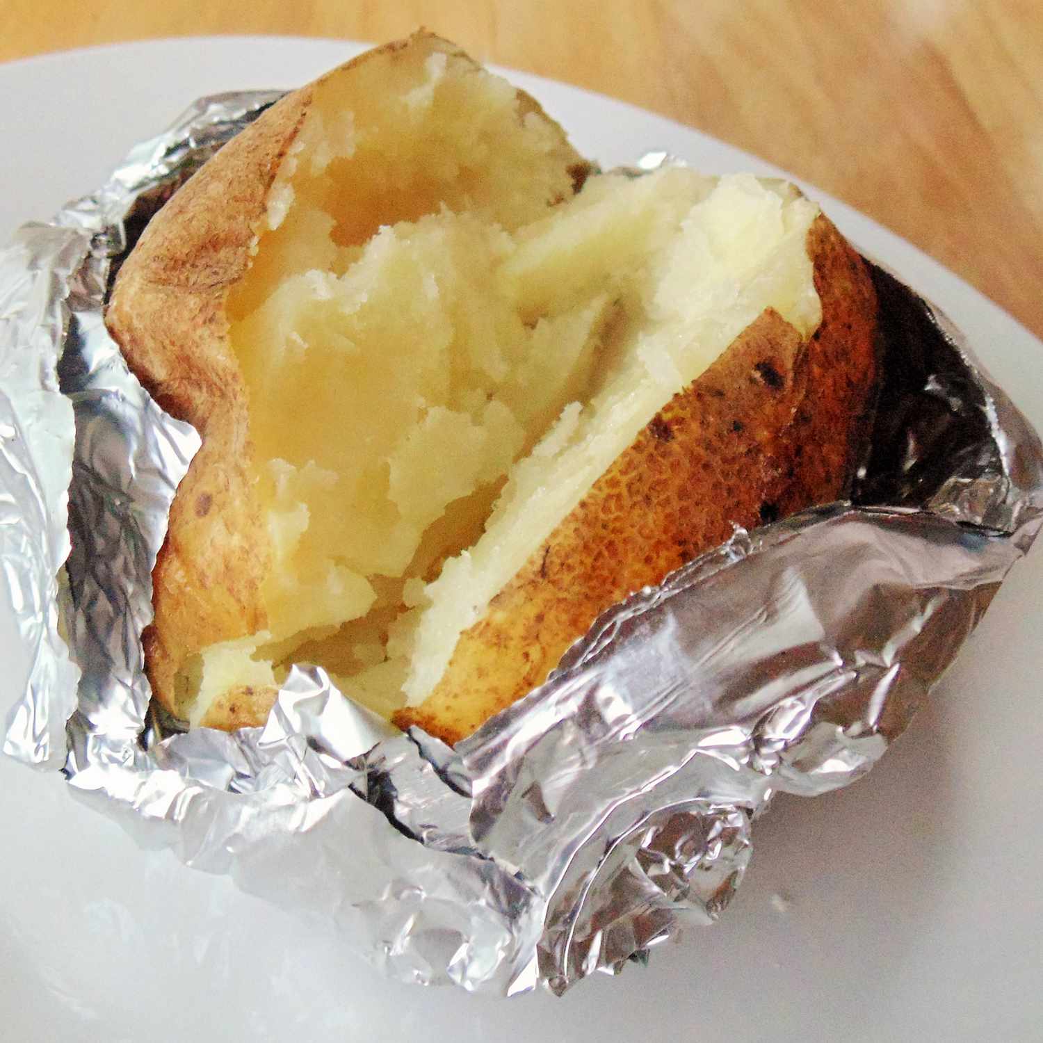 close up view of a baked cut in half wrapped with aluminum foil on a plate