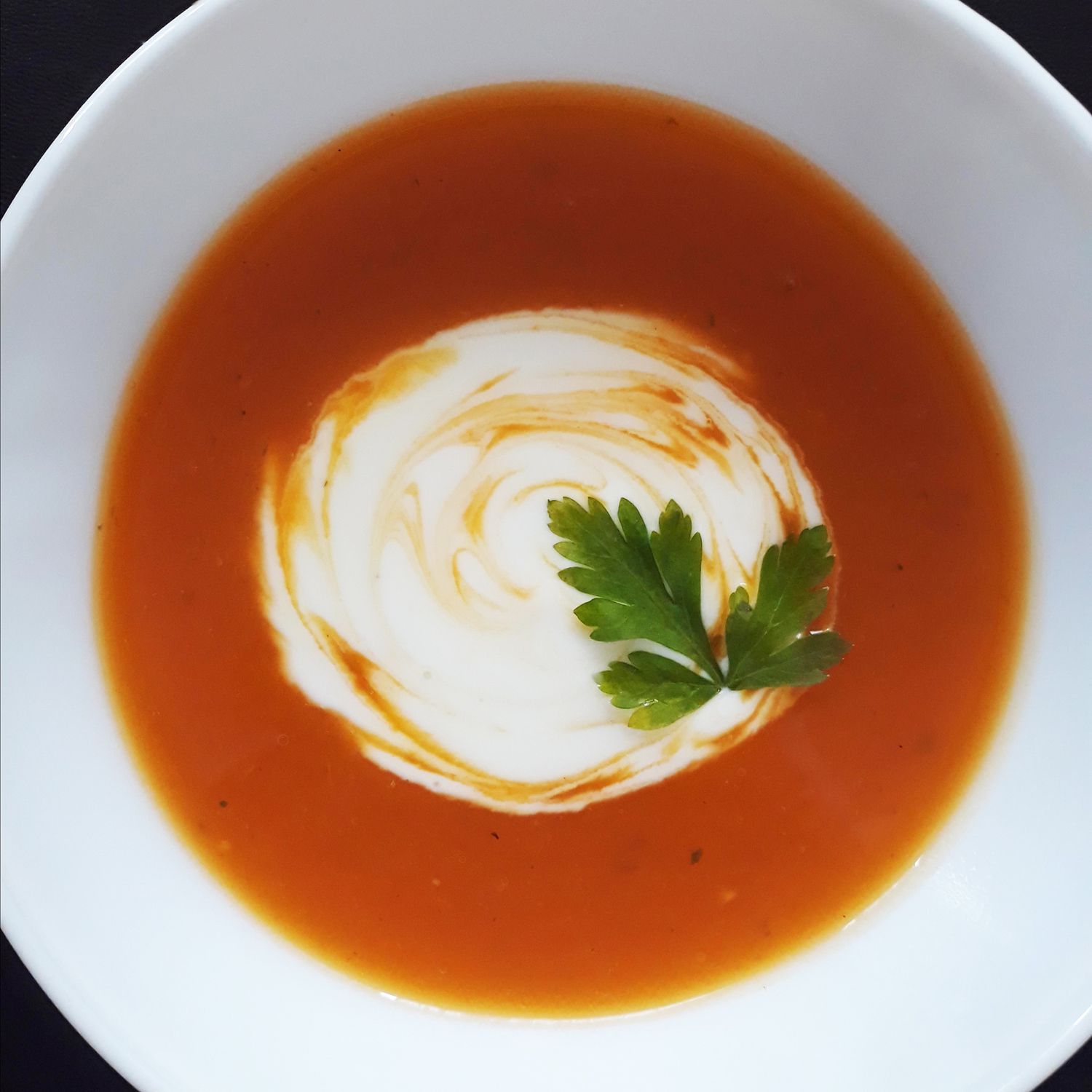 overhead view of Pumpkin Soup with cream and herbs in a bowl