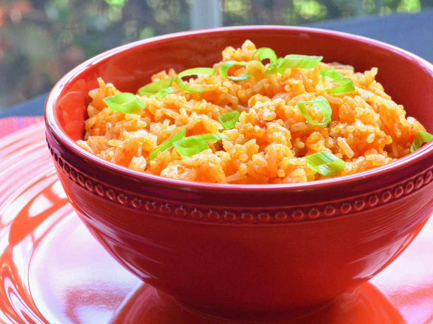 close of up view of Mexican rice garnished with green onions in a red bowl