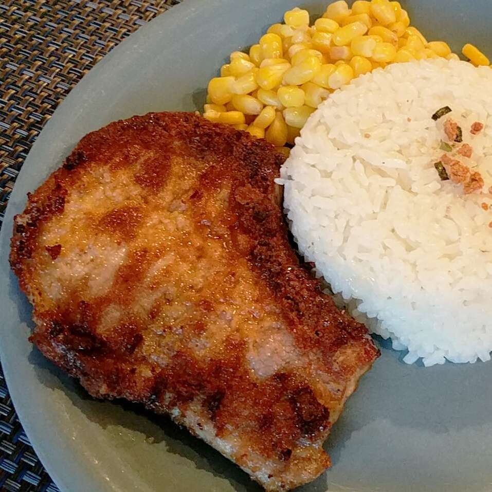close up view of oven-fried pork chops on a plate with rice and corn