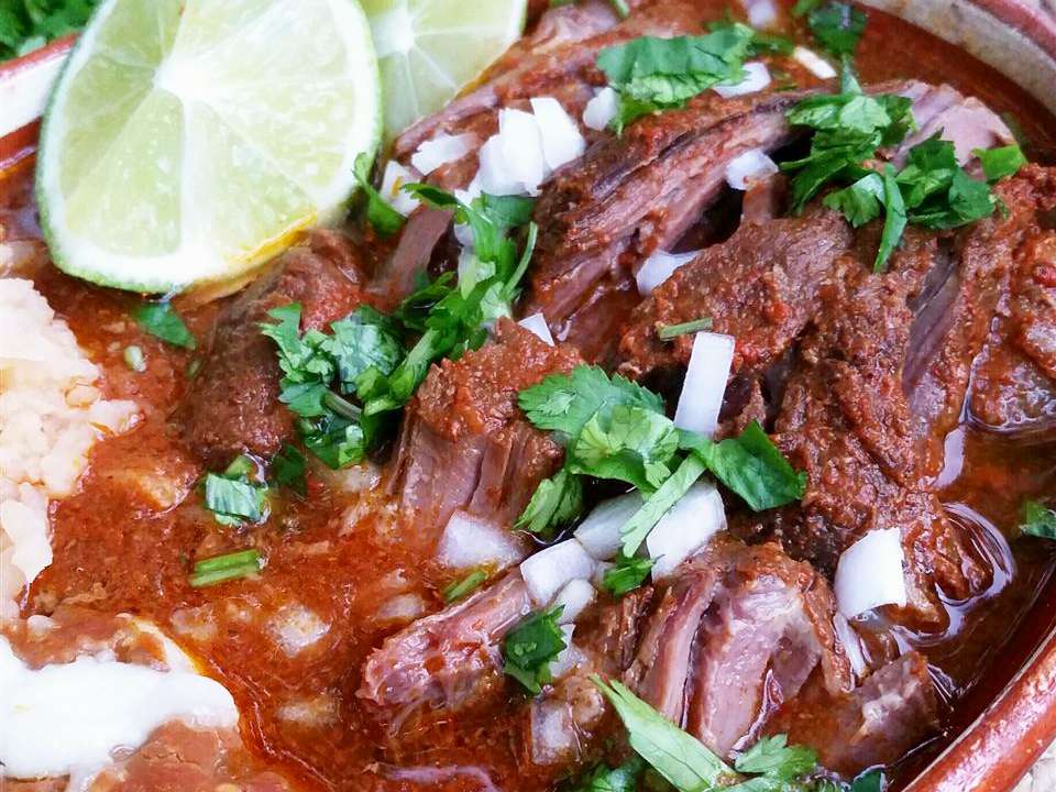 close up view of Birria garnished with herbs and lime bedges