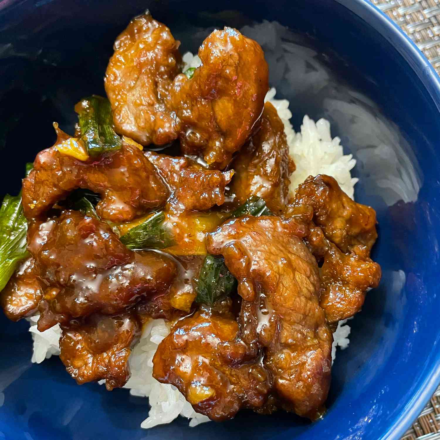 close up view of Mongolian Beef and Spring Onions over rice in a blue bowl