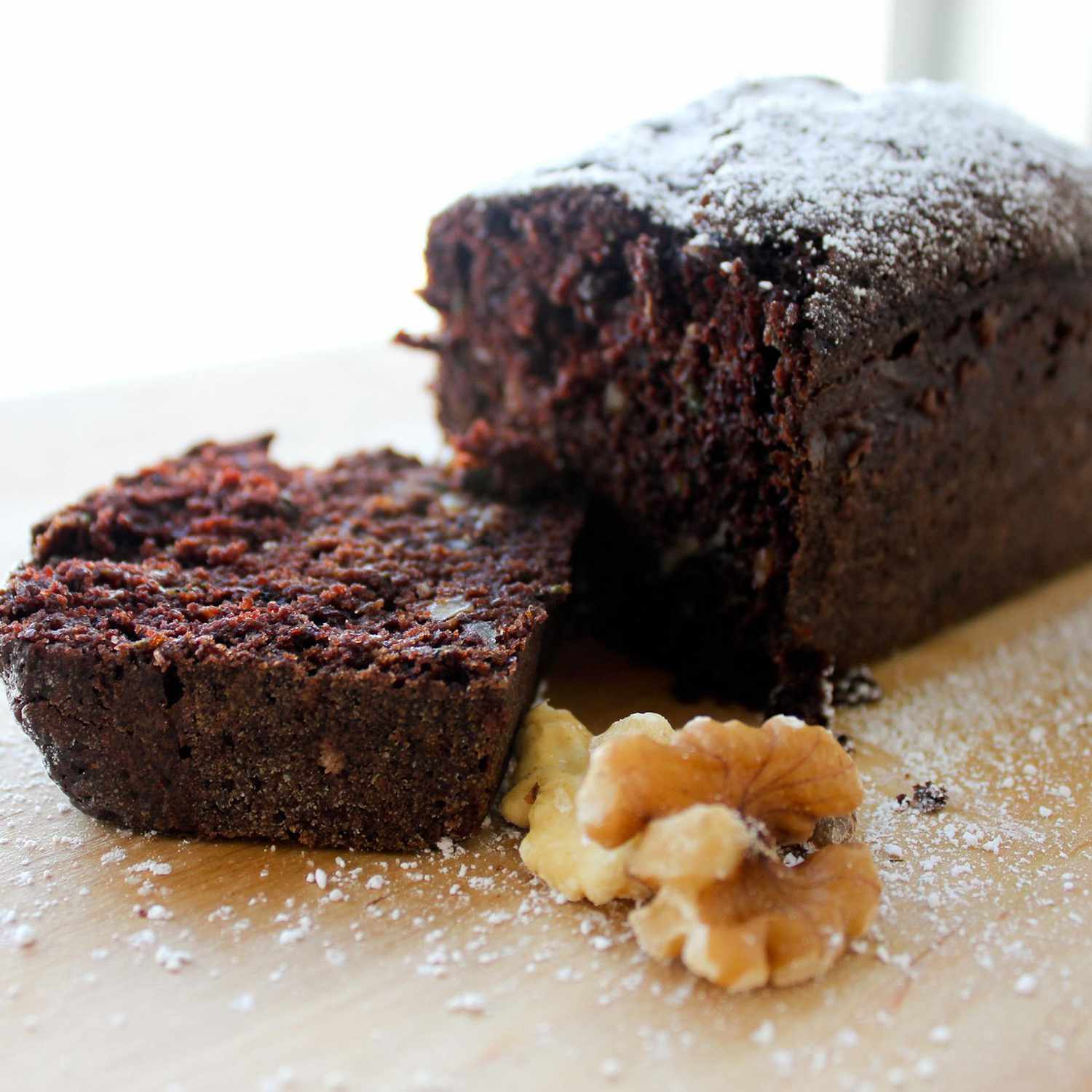 close up view of Chocolate Zucchini Cake garnished with powdered sugar, next to a walnut