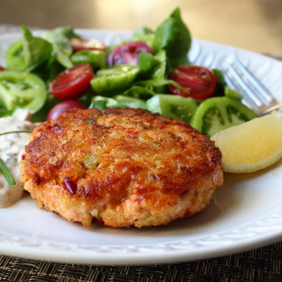 close up view of a Salmon Cake with salad and a lemon wedge on a plate