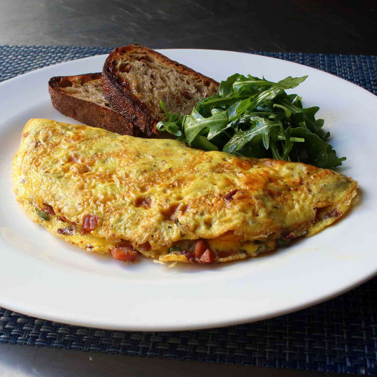 close up view of a Denver omelet with toast and an arugula salad on a plate