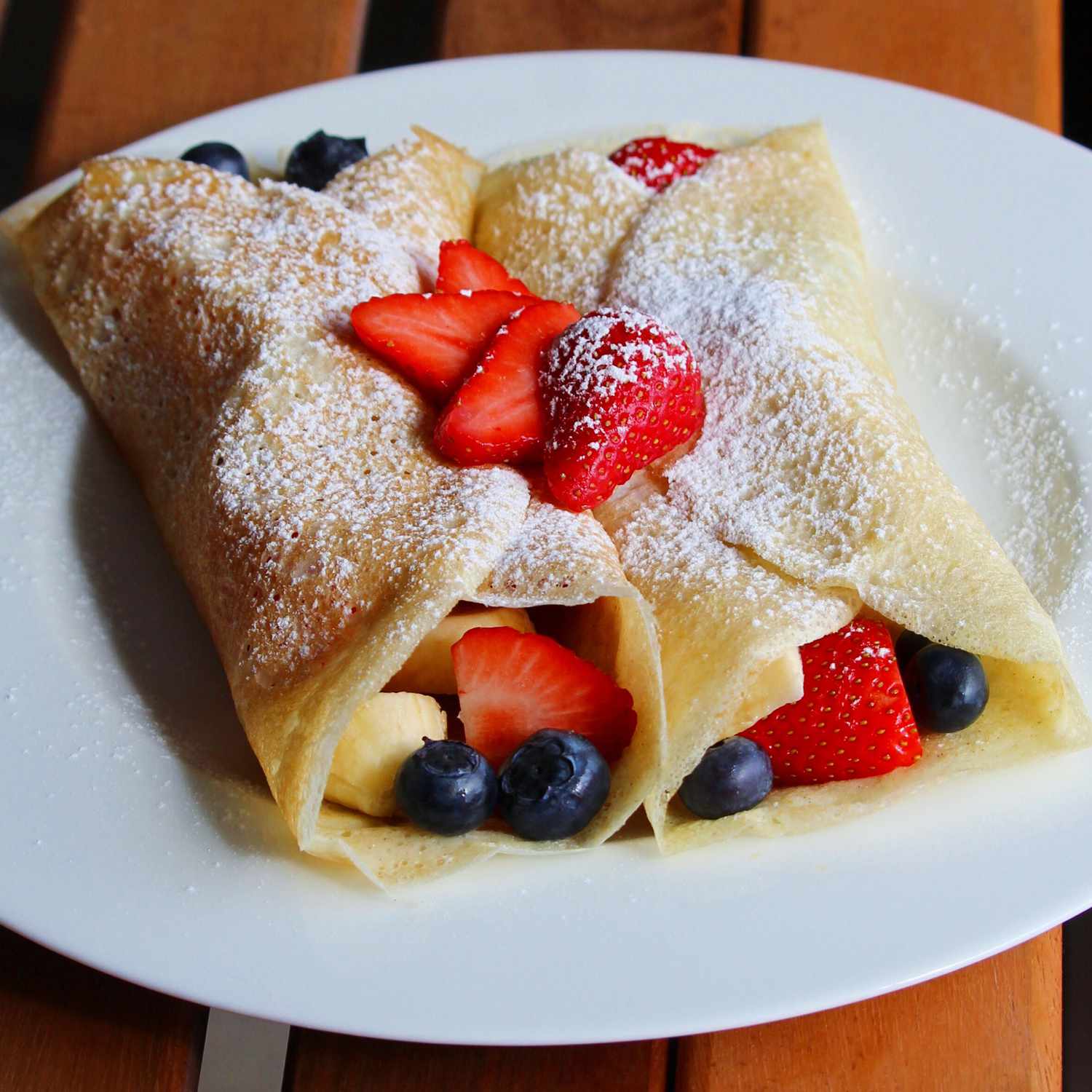 close up view of Dessert Crepes on a plate, topped with powdered sugar and berries