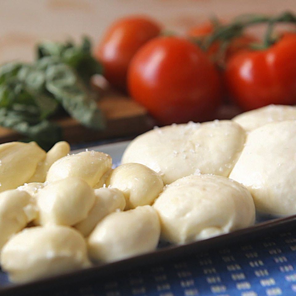 close up view of Homemade Mozzarella Cheese on a platter, with tomatoes and basil in the background