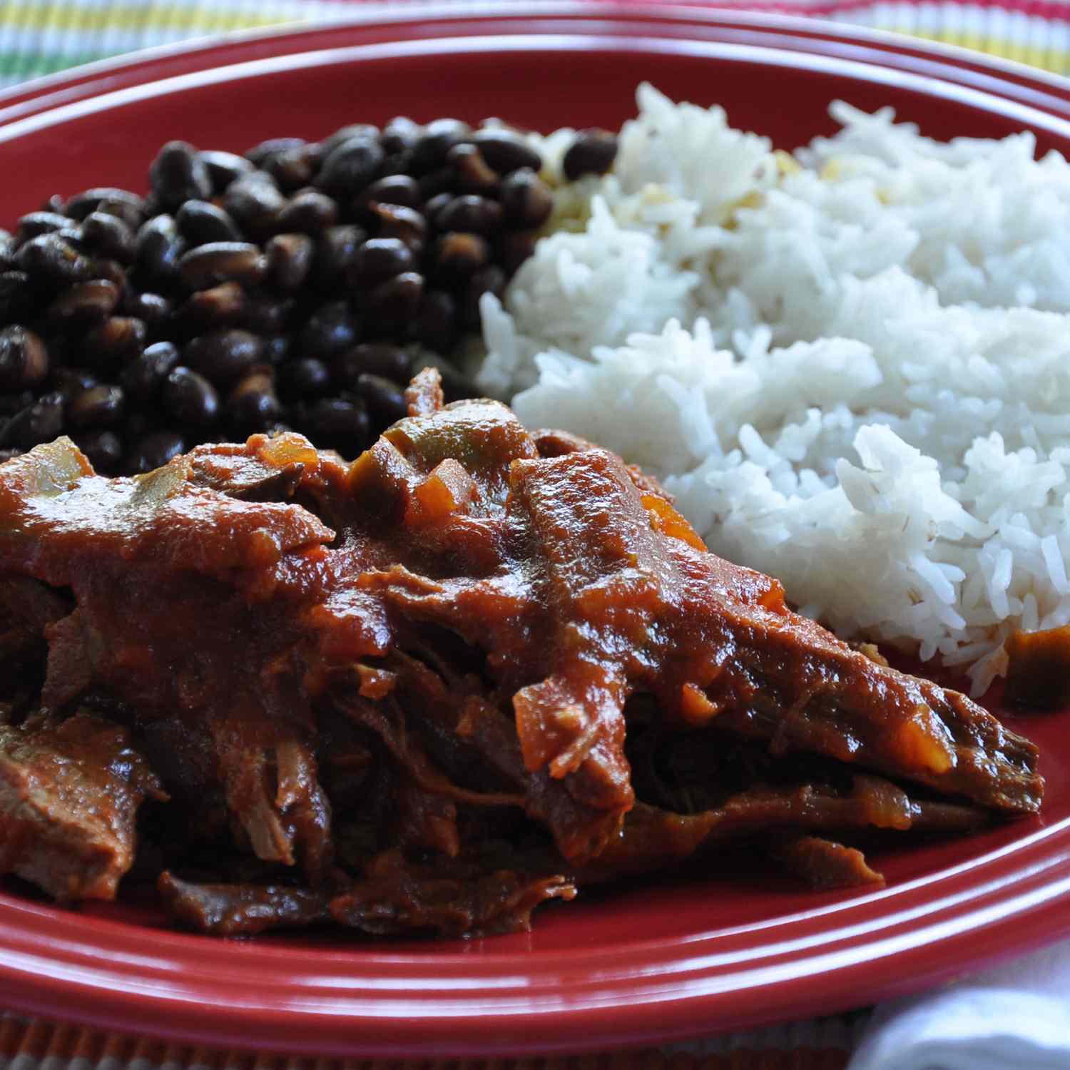 close up view of Cuban Ropa Vieja, rice and black beans on a red plate