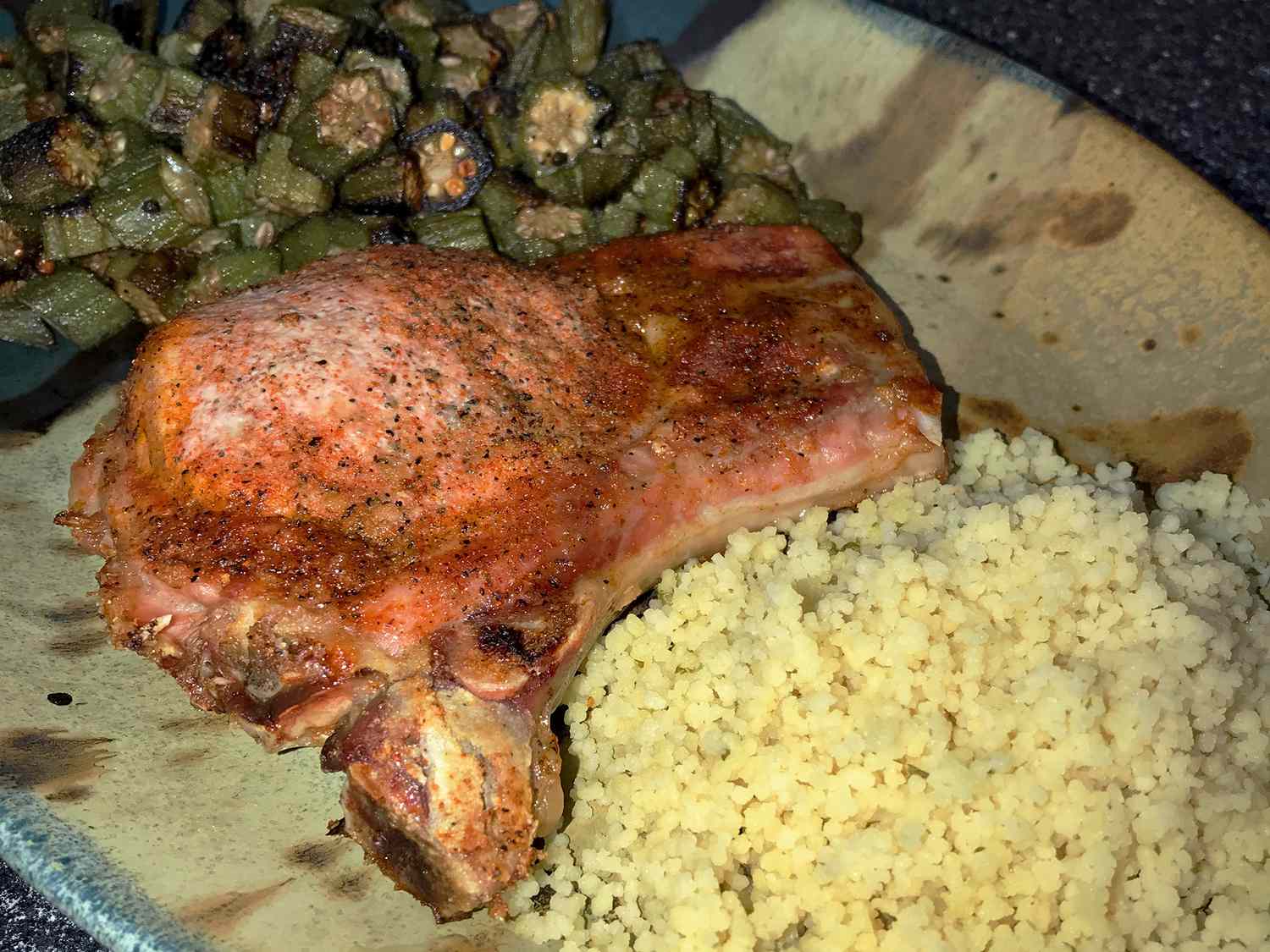 close up view of a baked pork chop, couscous and okra